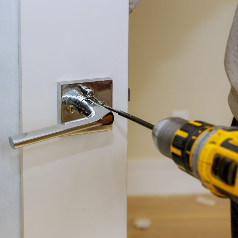 Carpenter installing door lock in the new house with a screwdriver